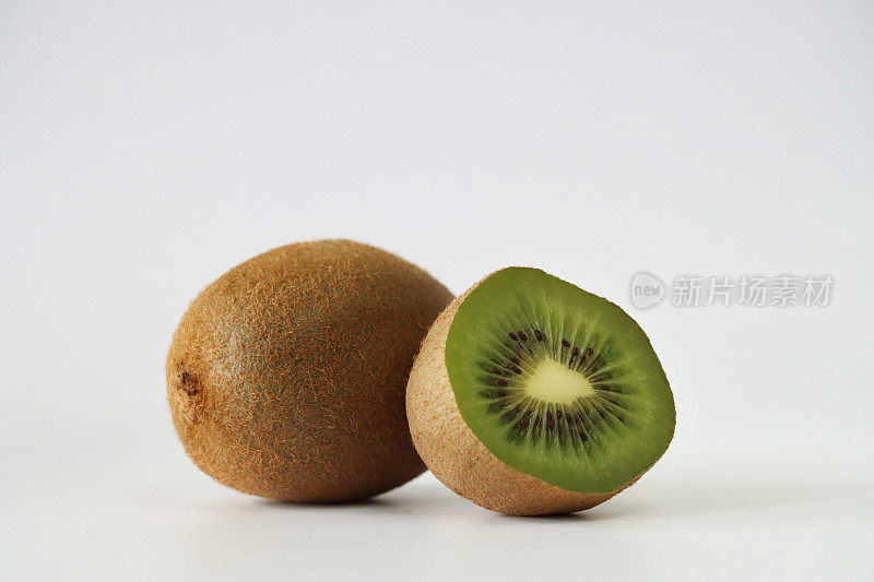整个猕猴桃(Actinidia chinensis)的图像，一半的中国醋栗显示模糊的棕色皮肤和亮绿色的果肉，黑色的种子环，白色背景，重点在前景，复制空间